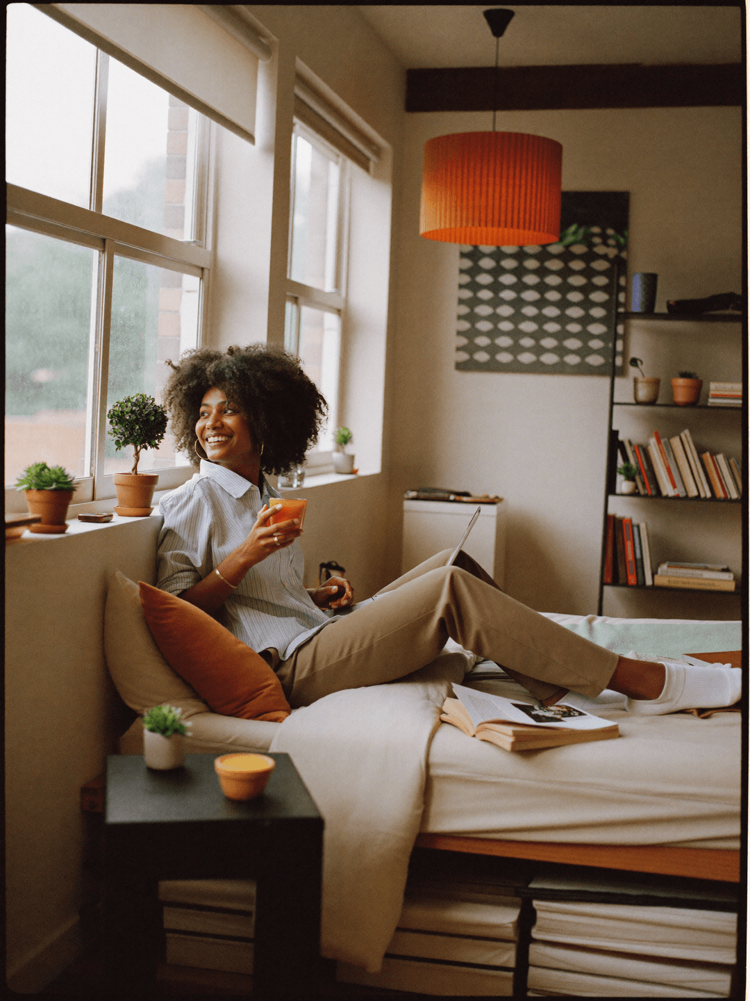 A student relaxing by the window of a tidy, warmly lit shared room